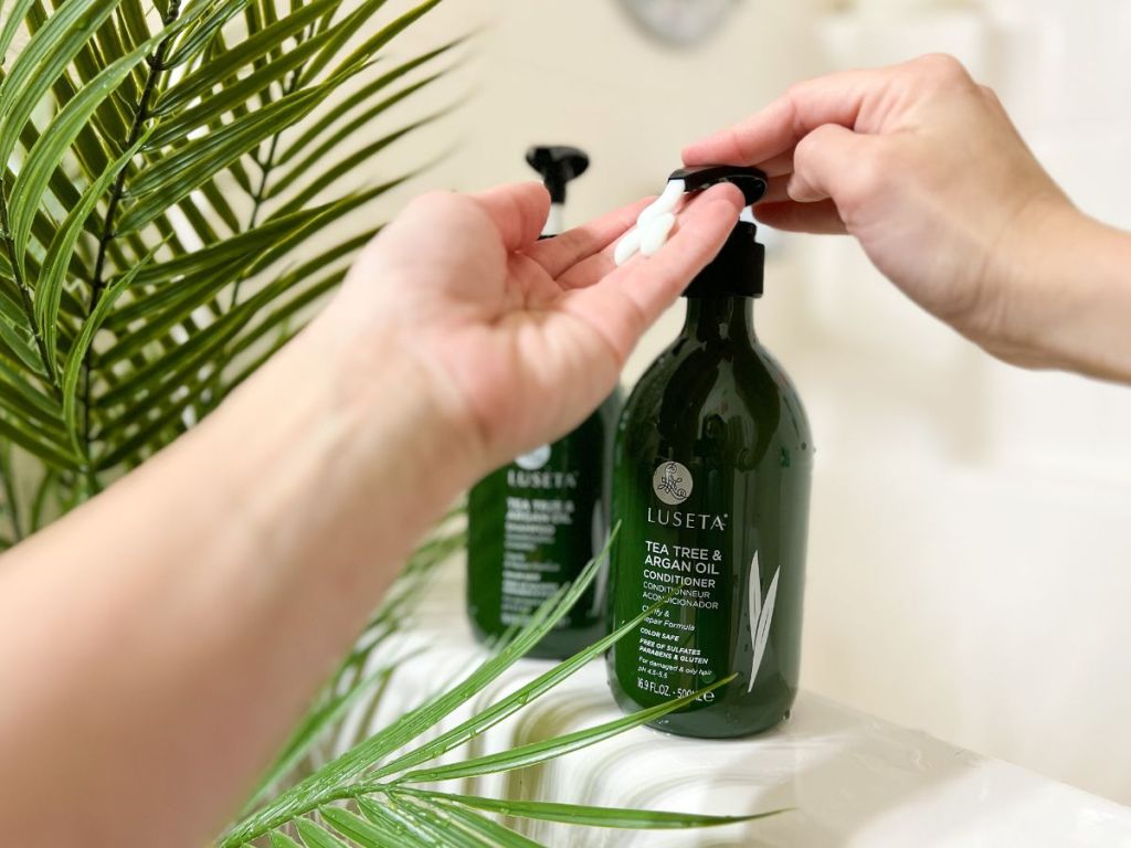 Luseta tea tree shampoo and conditioner sitting on side of bathtub with person pumping conditioner into hand