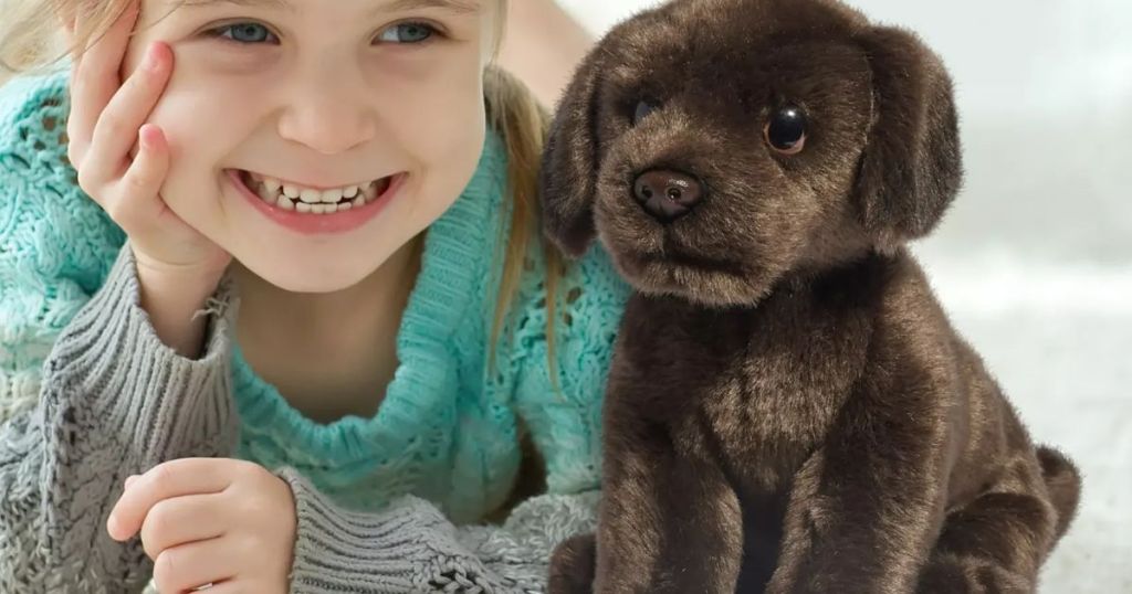 A little girl with a small stuffed brown Labrador toy dog