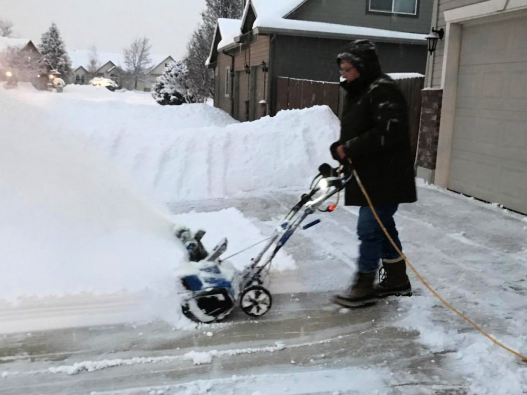 Man blowing snow on driveway using a corded snow blower
