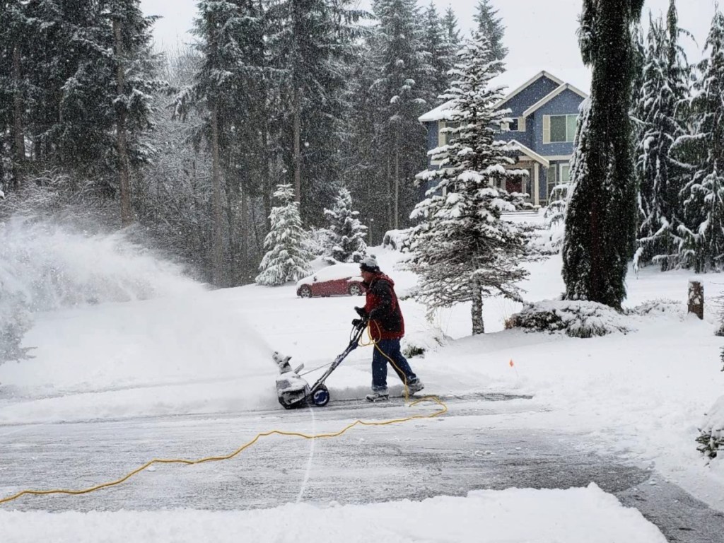 Man outside on driveway, blowing snow with electric snow blower