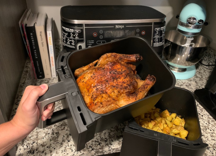 hand holding Ninja air fryer basket with whole roasted chicken inside