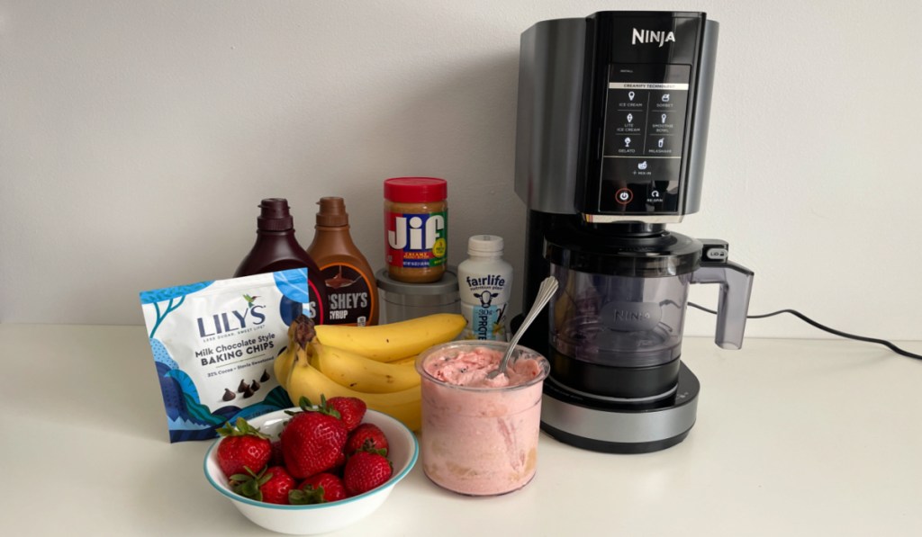 A Ninja CREAMi ice cream maker on a counter next to mix-ins and syrups