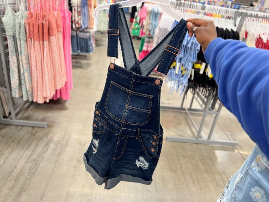 Hand holding a pair of shortalls on a hanger