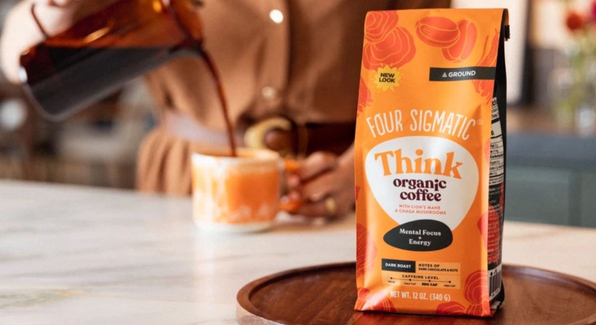 Bag of Organic Ground Mushroom Coffee by Four Sigmatic Dark Roast, Fair Trade Gourmet Coffee with Lion's Mane, Chaga & Mushroom Powder on a counter with woman pouring a cup of coffee in the background
