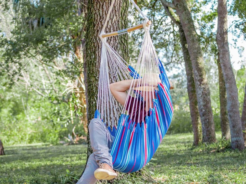woman sitting in blue and striped hammock chair hanging from tree
