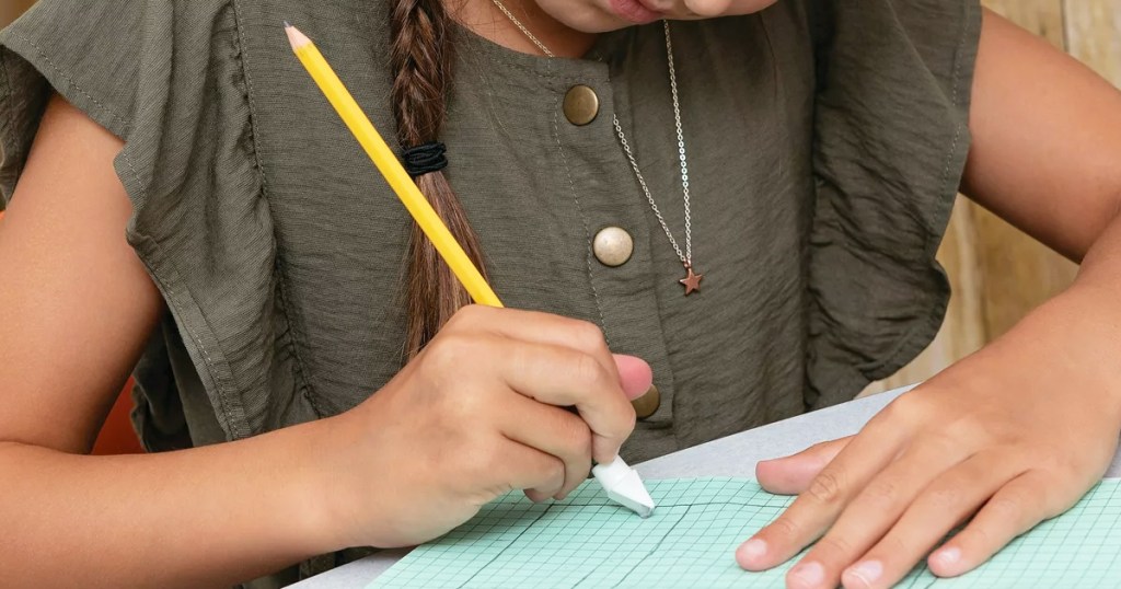 girl using white pencil cap eraser in blue notebook
