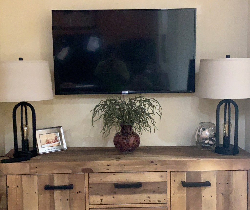 tv mounted on wall above tv stand with two lamps on either side