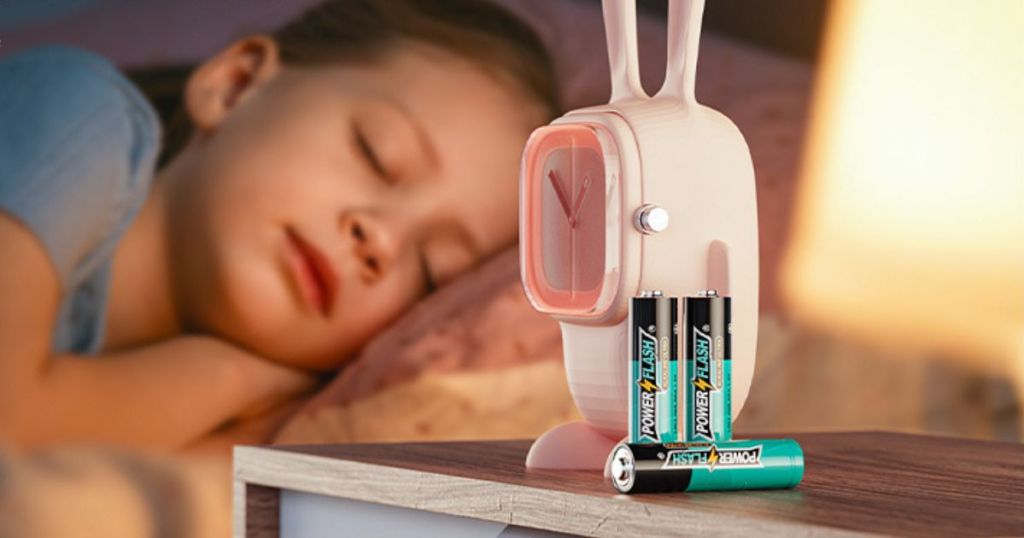 batteries on end table next to pink clock with kid sleeping on bed