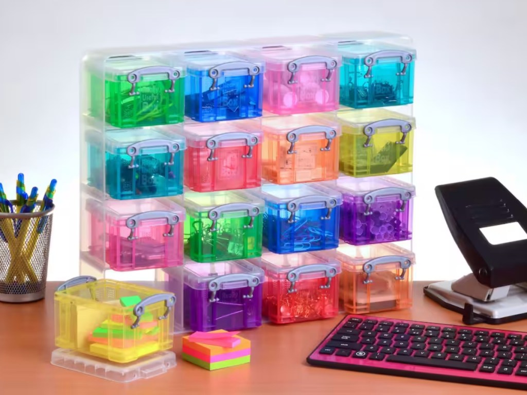 16 multicolored boxes on desktop next to pens and keyboard