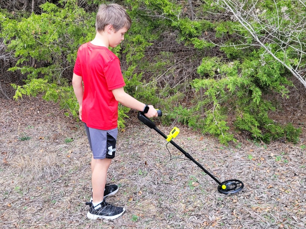 boy using a metal detector in grass