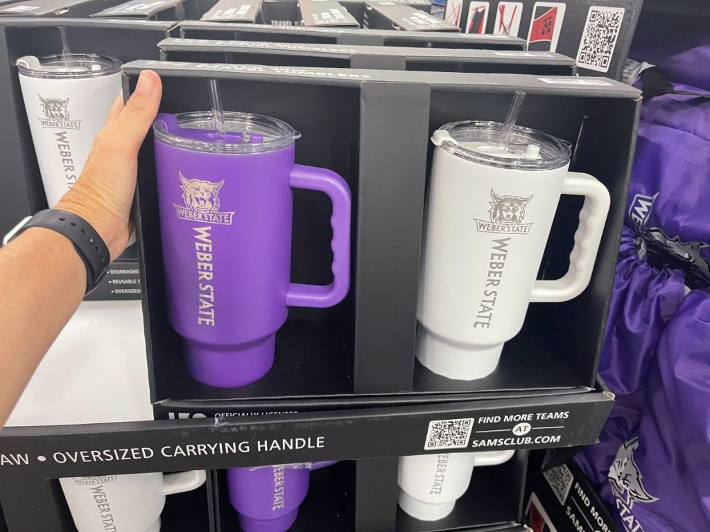 A hand grabbing a box with 2 large tumblers in white and purple