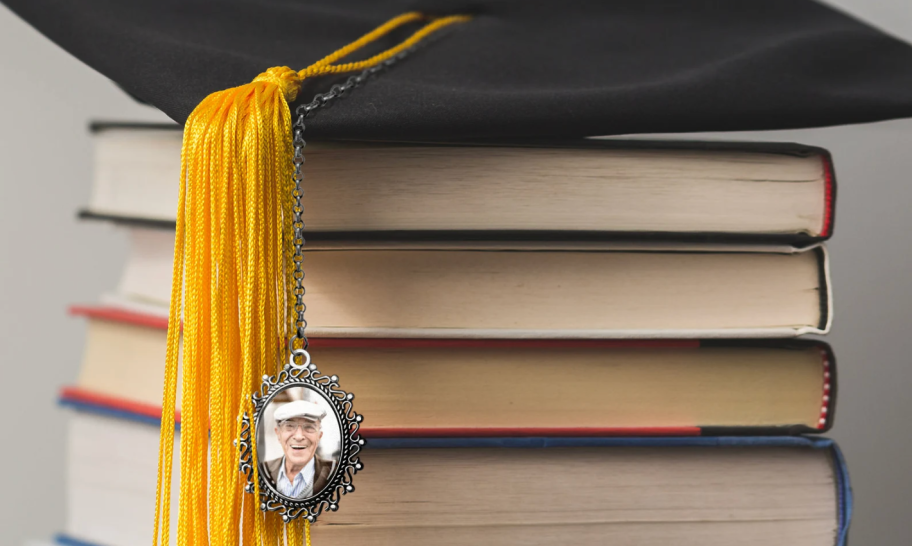 graduation hat sitting on books with gold tassel and photo hanging