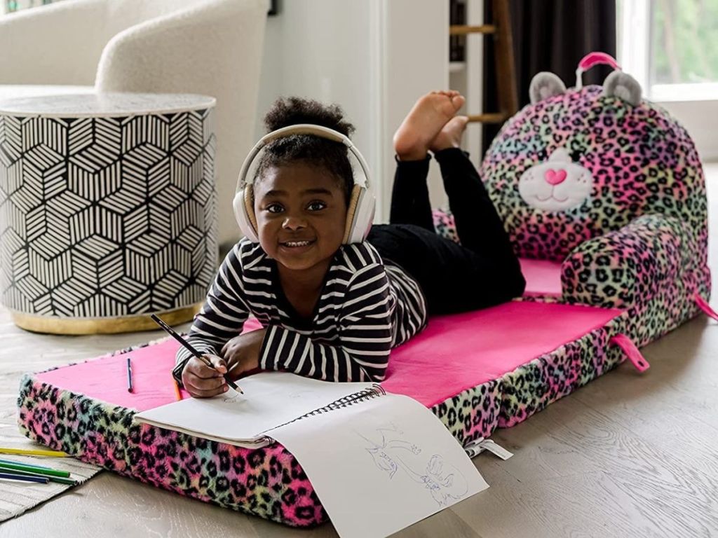 Little girl laying on her stomach while doing her homework on a Soft landings Leopard chair bed.