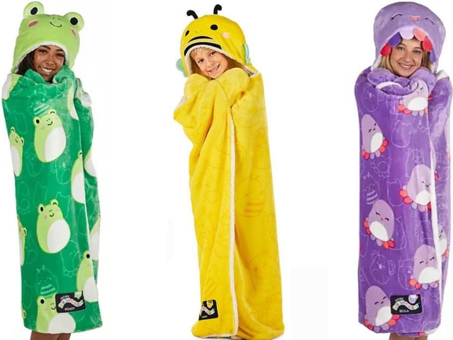 Stock images of kids wearing frog, bee and octopus squishmallows hooded wearble throw blankets