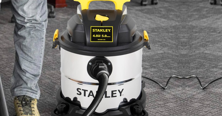 person using a silver and black Stanley wet/dry vac on carpeted floors