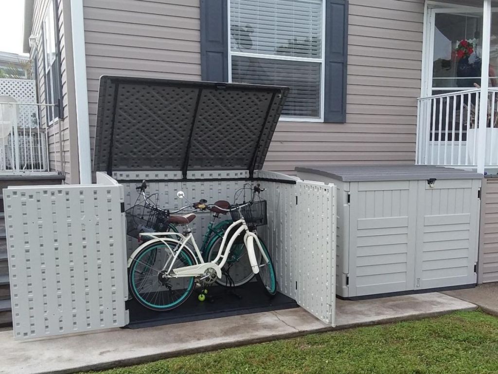 two suncast storage sheds outside of a home with one open containing bikes and another closed next to it