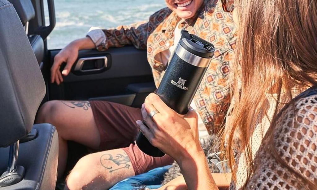 a woman in a bronco holding The Aerolight Transit Bottle 20oz in black
