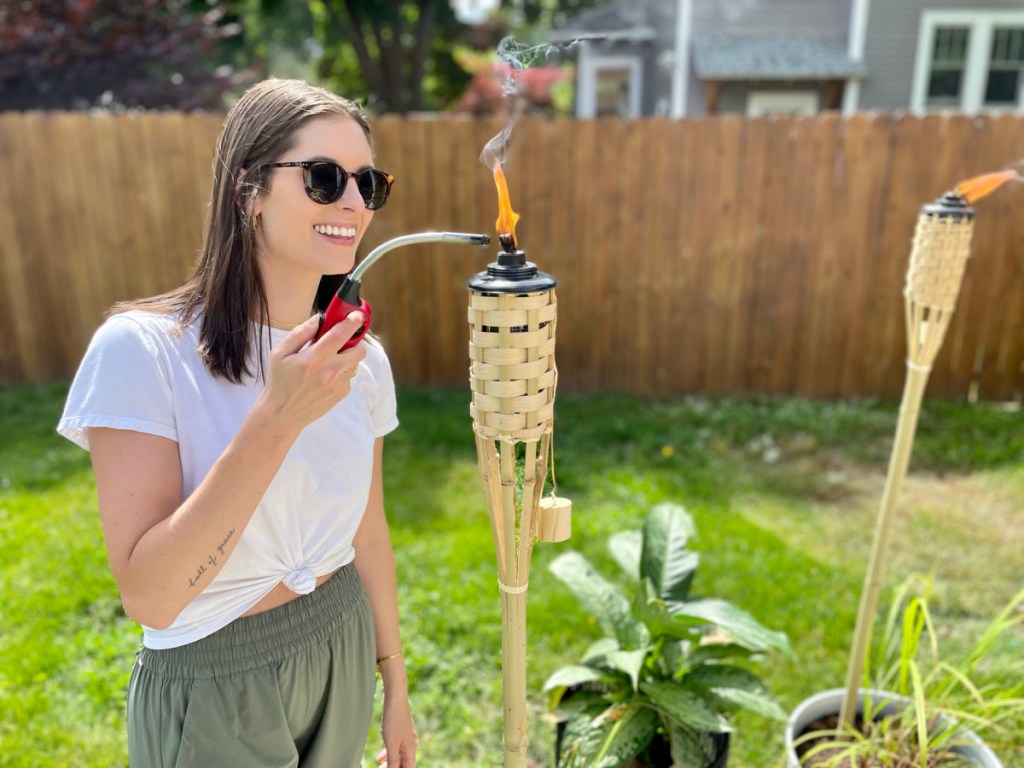 Woman in her backyard lighting Tiki torches from Walmart