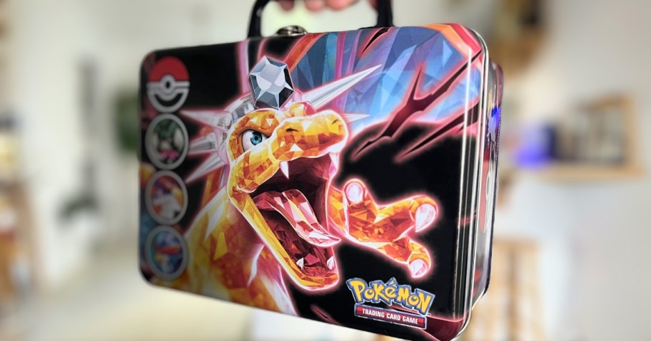 hand holding a metal Pokemon collectors tin with Charizard on the cover