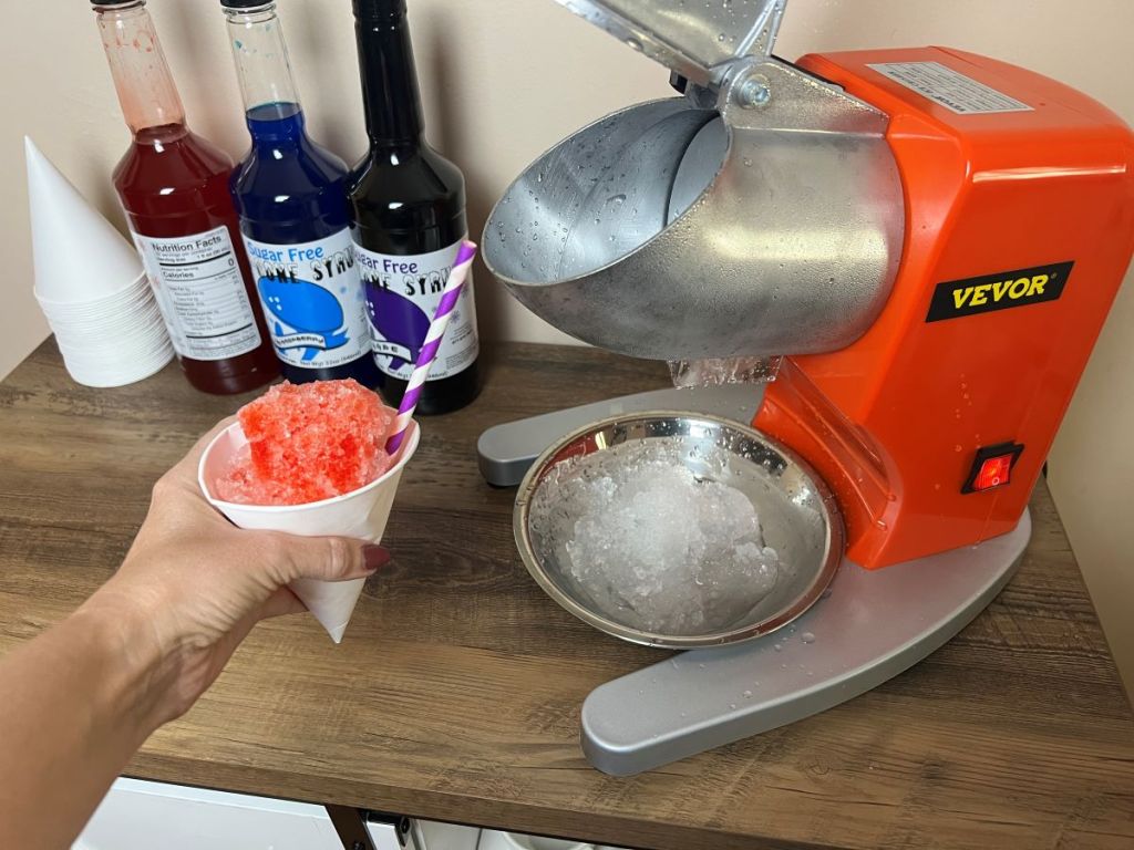 Hand holding a sno cone next to an ice crusher machine