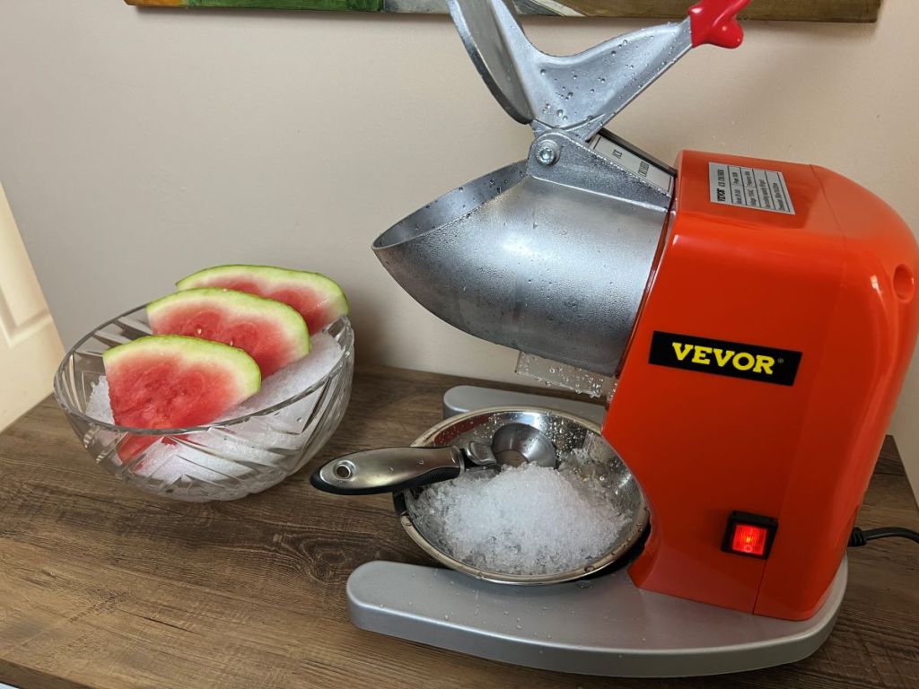 Ice shaver with a bowl of ice and watermelon slices next to it