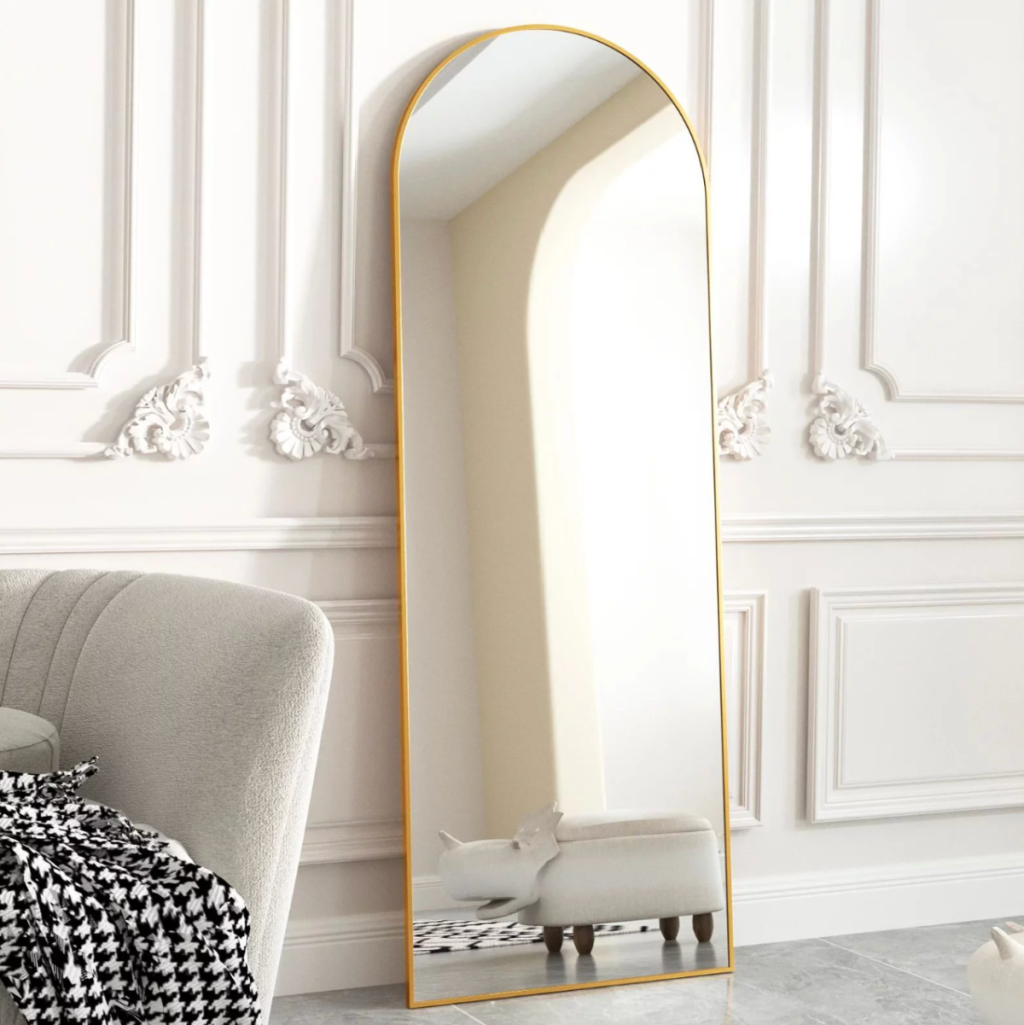 A gold arched wall mirror from BEAUTYPEAK leaning up against a wall