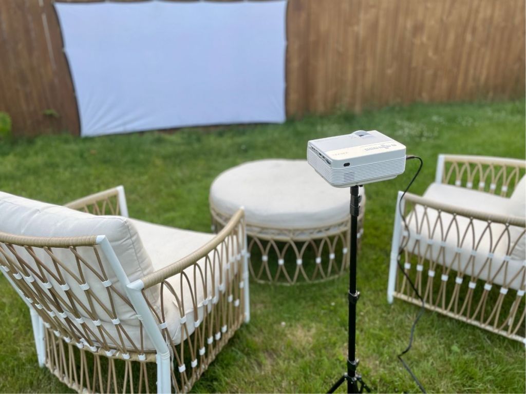 projector on tripod in backyard in front of fabric by fence