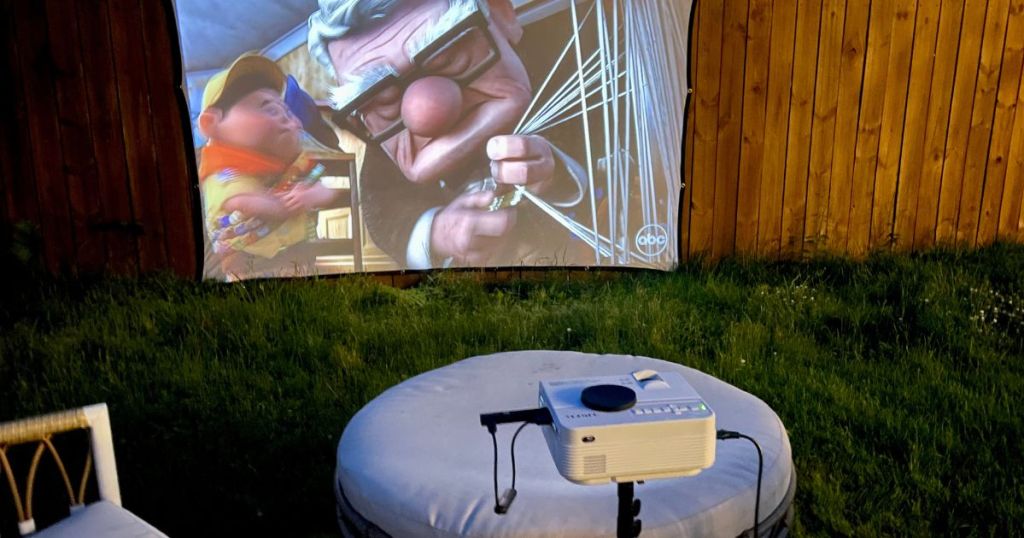 projector on tripod in backyard projecting "UP" movie on fabric by fence