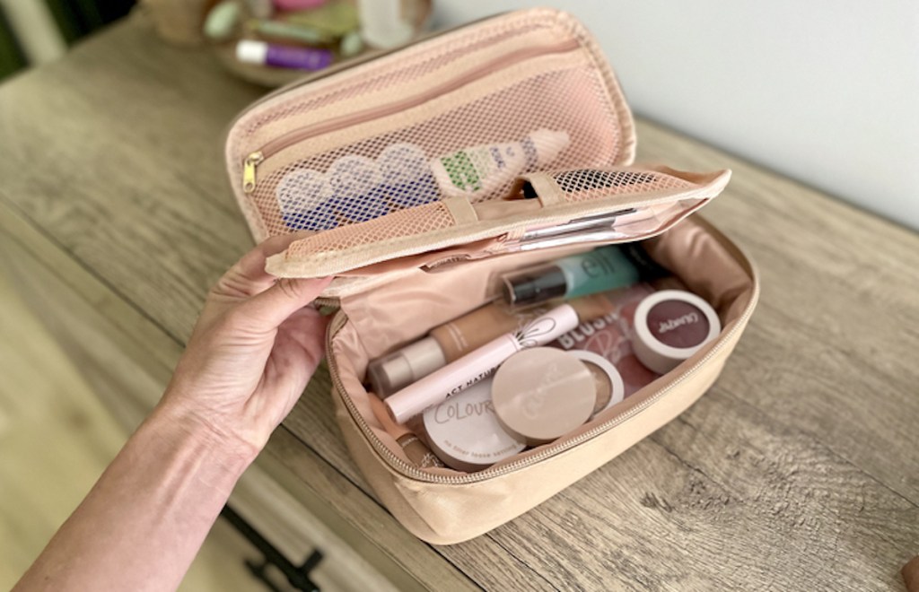 hand holding middle compartment of toiletry makeup bag on wood dresser