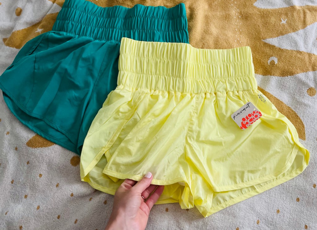 hand holding edge of yellow free people the way home shorts with avia shorts walmart underneath