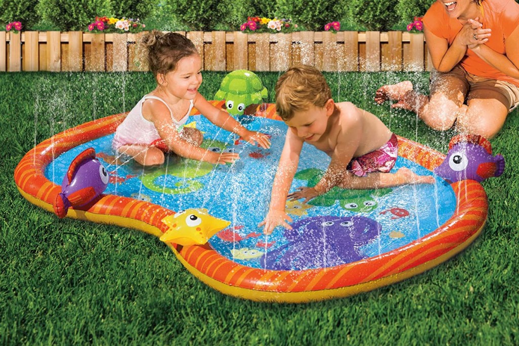 two toddlers on water mat next to mom