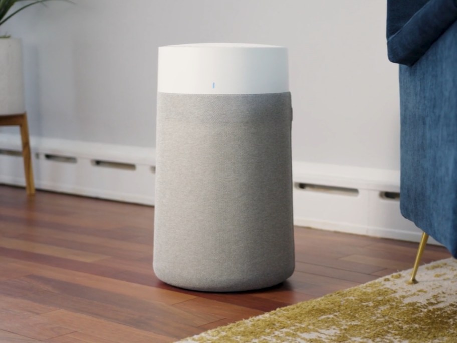 a medium size grey and white air purifier machine in a living room next to a blue chair