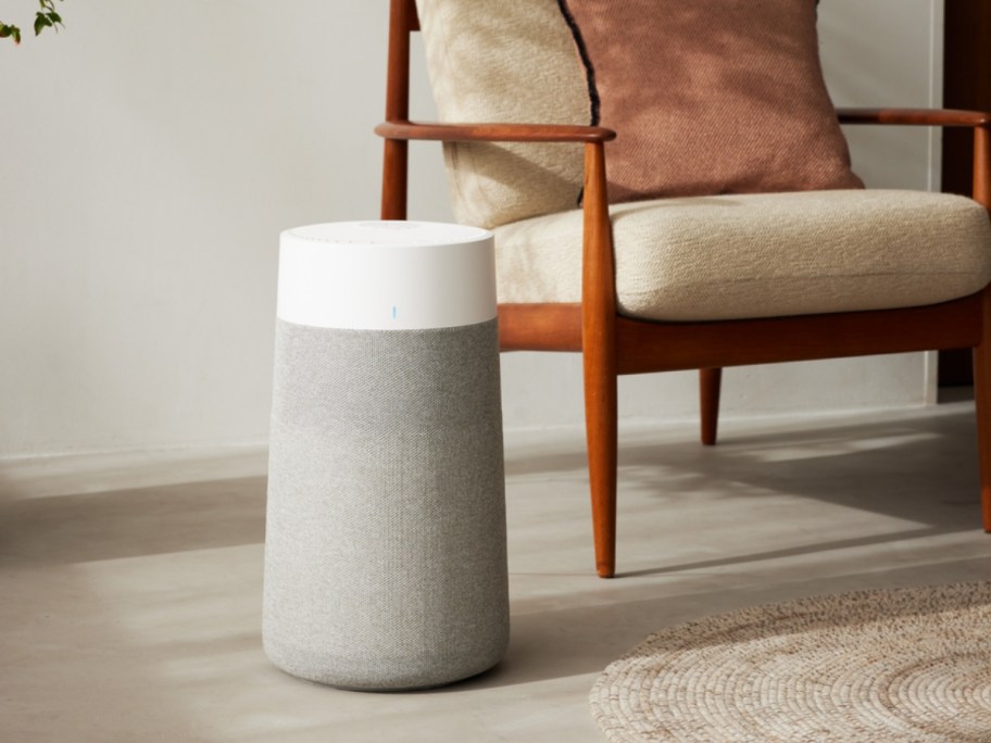 a medium size grey and white air purifier machine next to a wood and tan accent chair in a living room