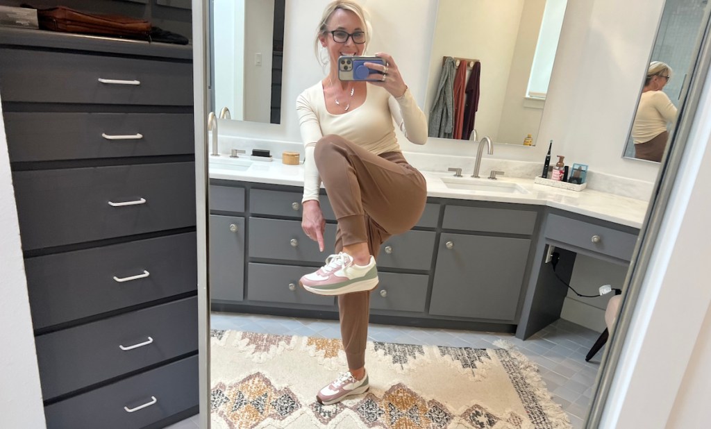woman holding up foot with sneaker in bathroom mirror