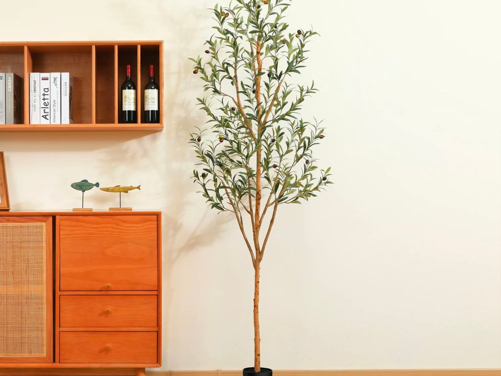 faux olive tree in white pot next to kitchen cabinets