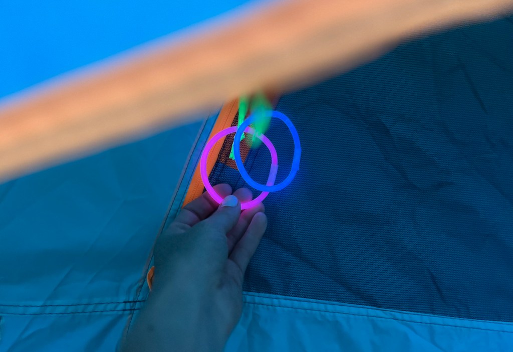 hand holding two glow sticks on blue and orange zipper tent