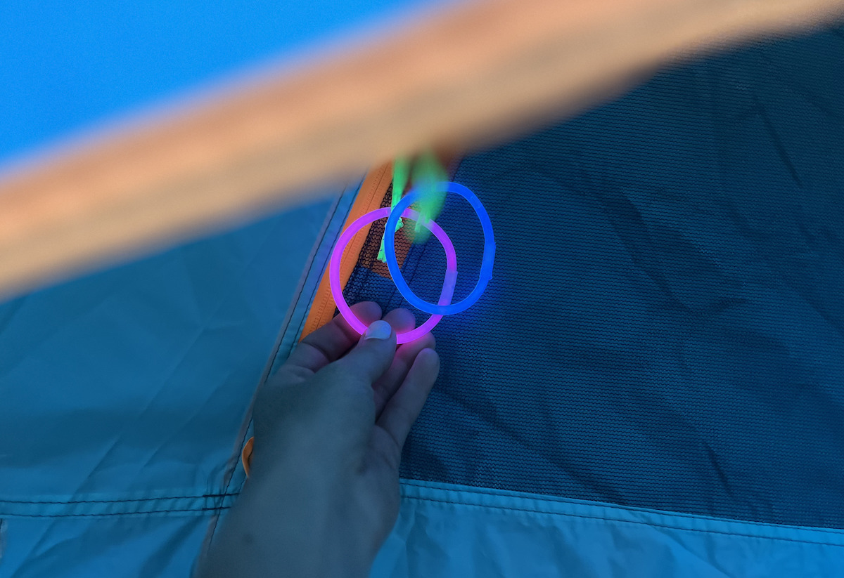 hand holding two glow sticks on blue and orange zipper tent