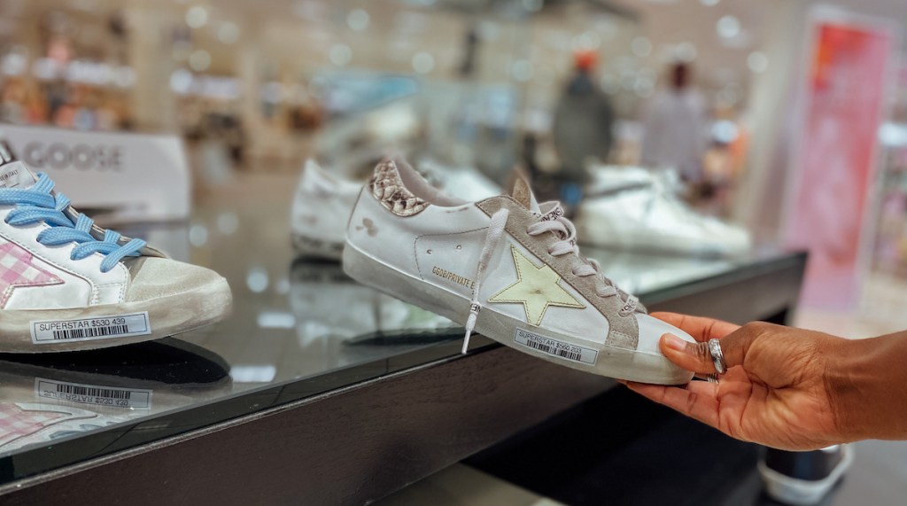 hand holding a golden goose sneaker in department store