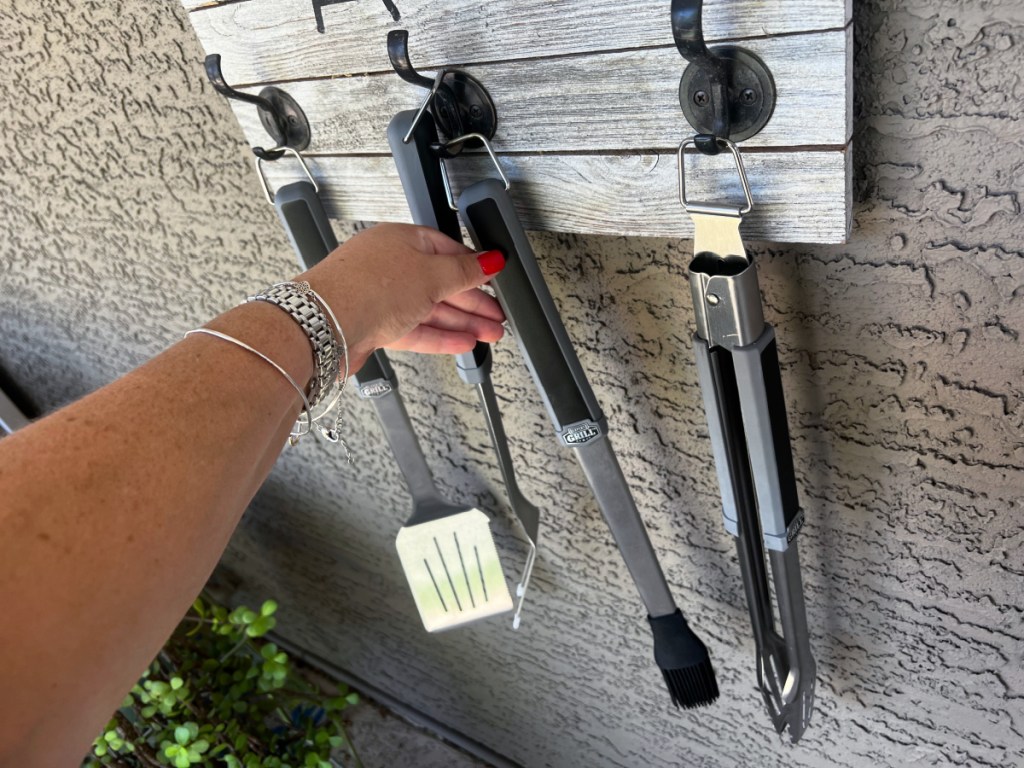 hand lifting a grilling tool off a wall display at home