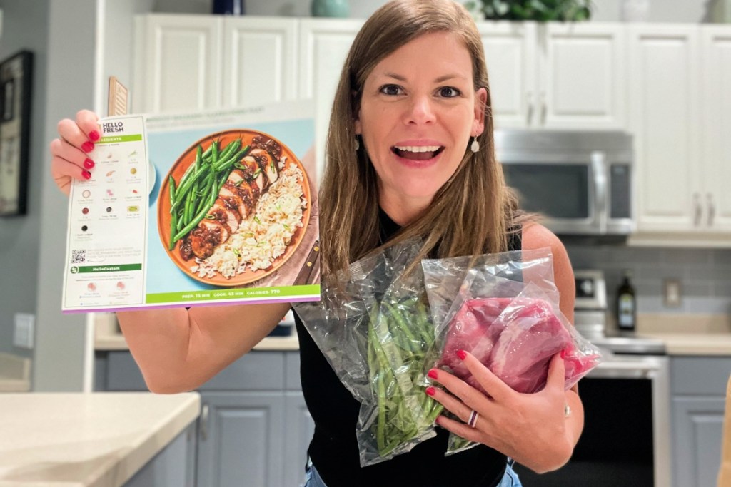 woman holding up hello fresh recipe cards and packaged ingredients