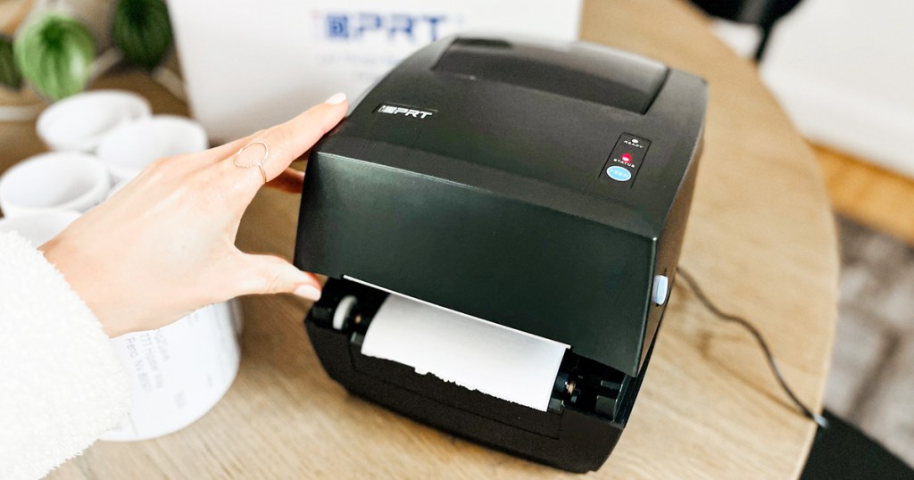 hand touching a black thermal label printer on wood table