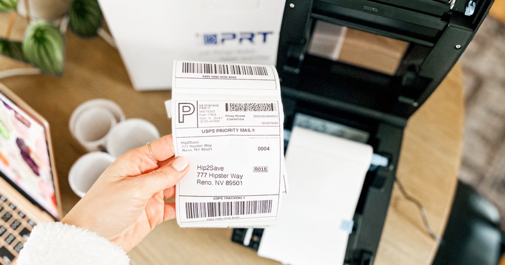 hand holding up a usps shipping label with thermal printer in background