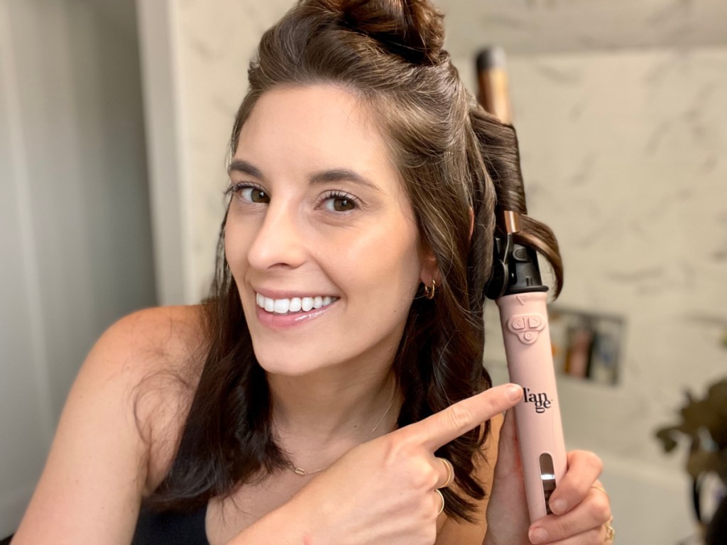 smiling woman pointing at the l'ange le pirouette curling iron she is using to style her hair