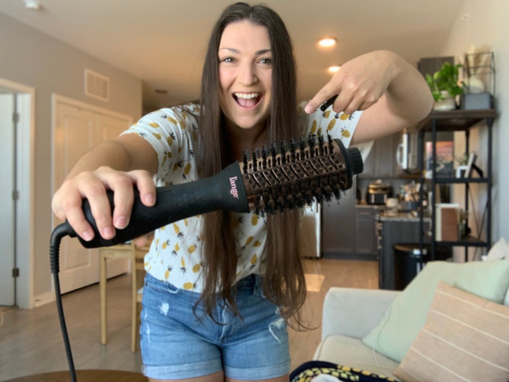 smiling woman holding and pointing to a lange le volume hair dryer brush in her hand
