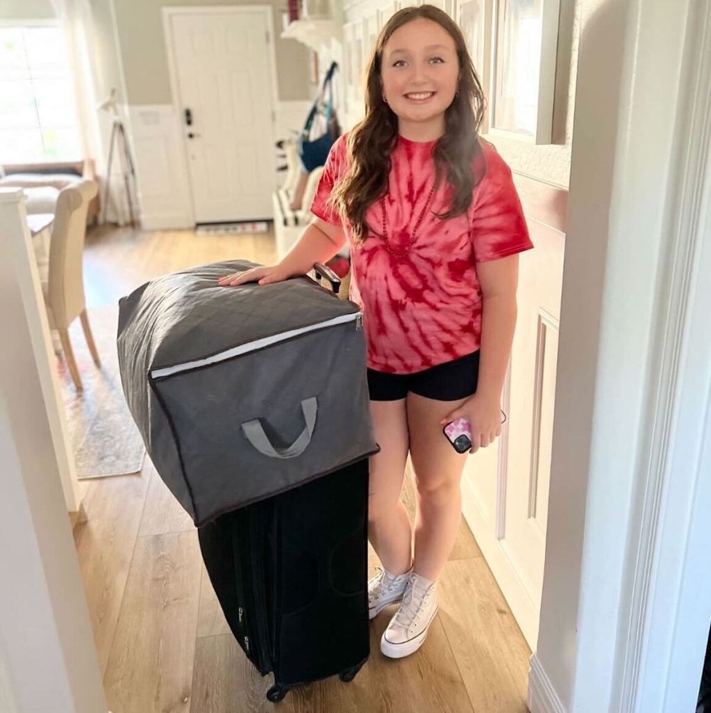 teen standing next to suitcase with bedding bag on top 