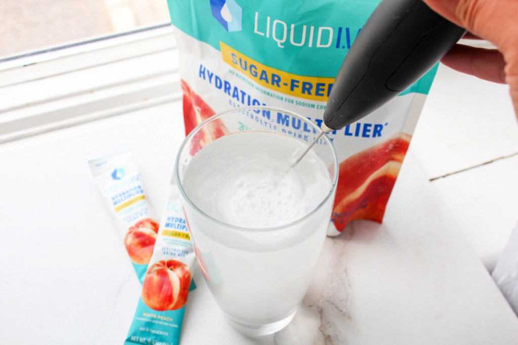 person using a hand frother to blend their liquid iv hydration sugar free packet into water