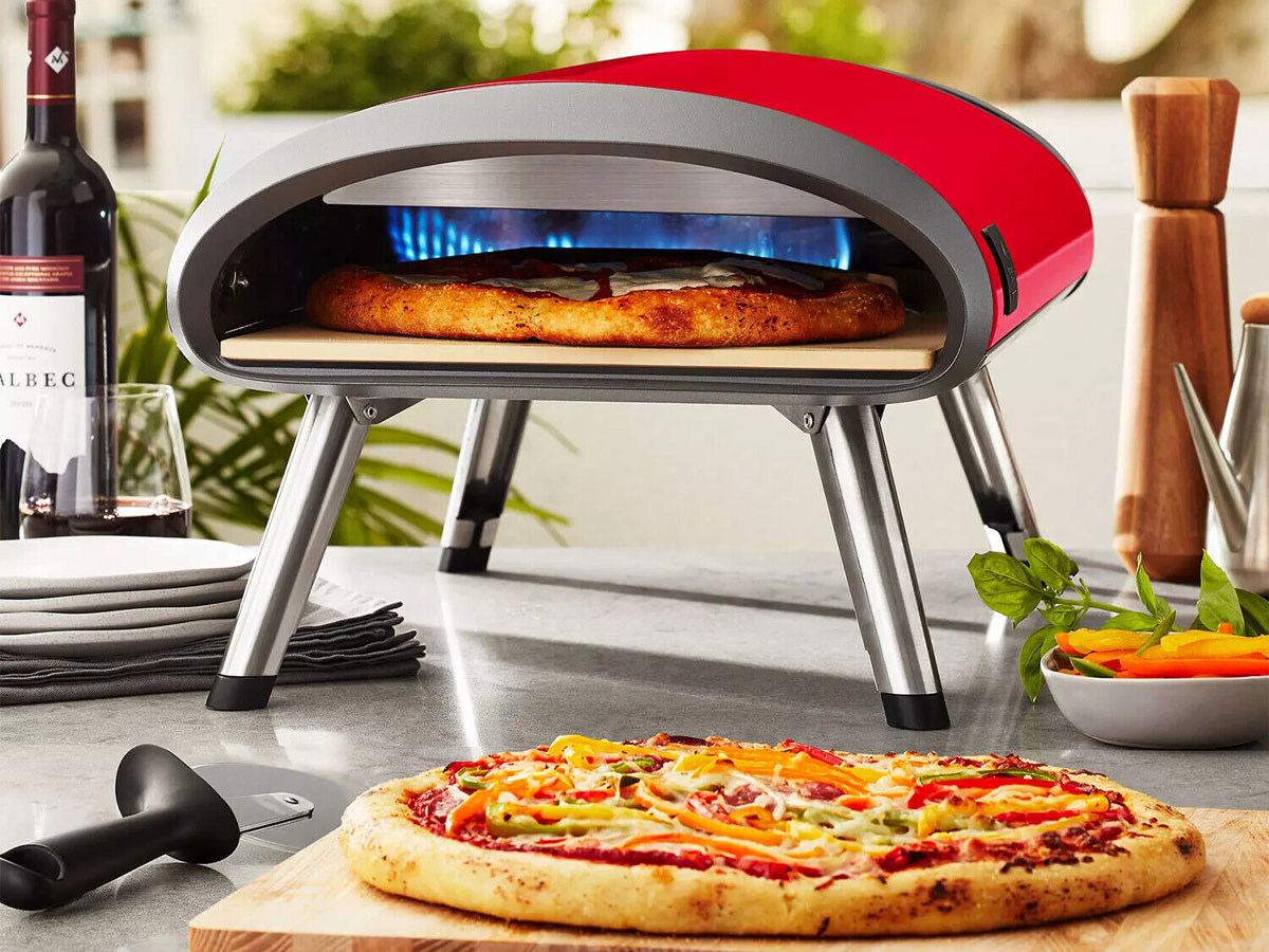 red pizza oven with pizza cooking inside and pizza on cutting board