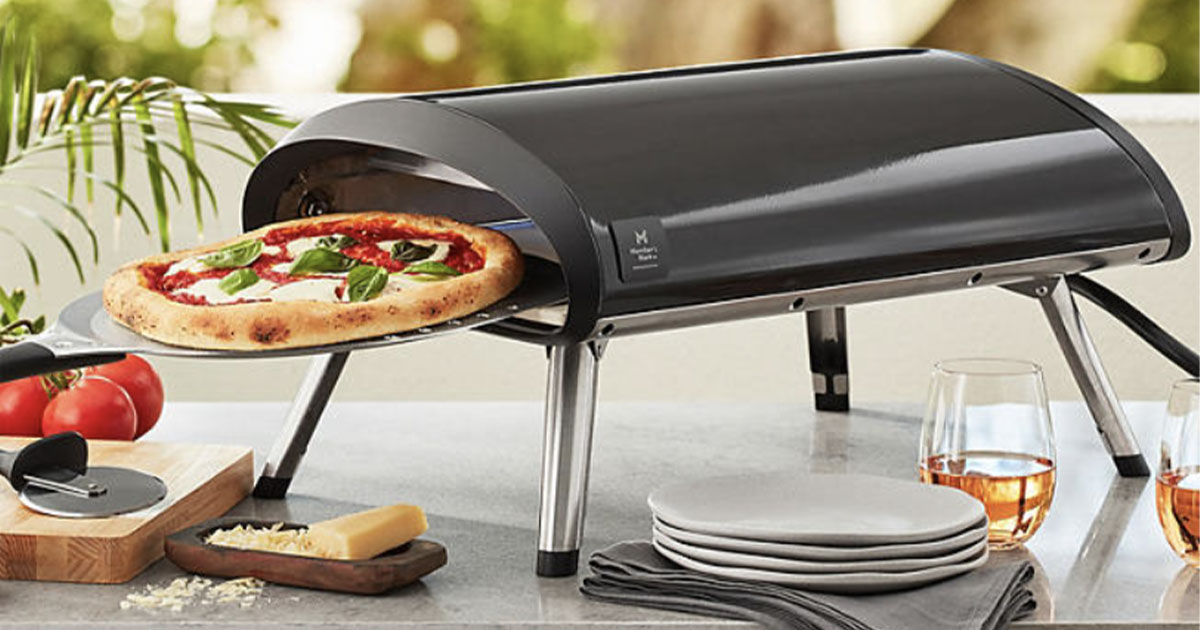 black pizza oven with pizza coming out of it on table with plates