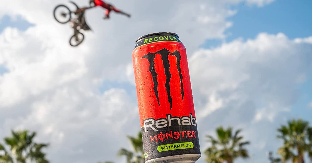  a close up of a can of monster rehab watermelon with a man on a bicycle doing a midair flip in the background