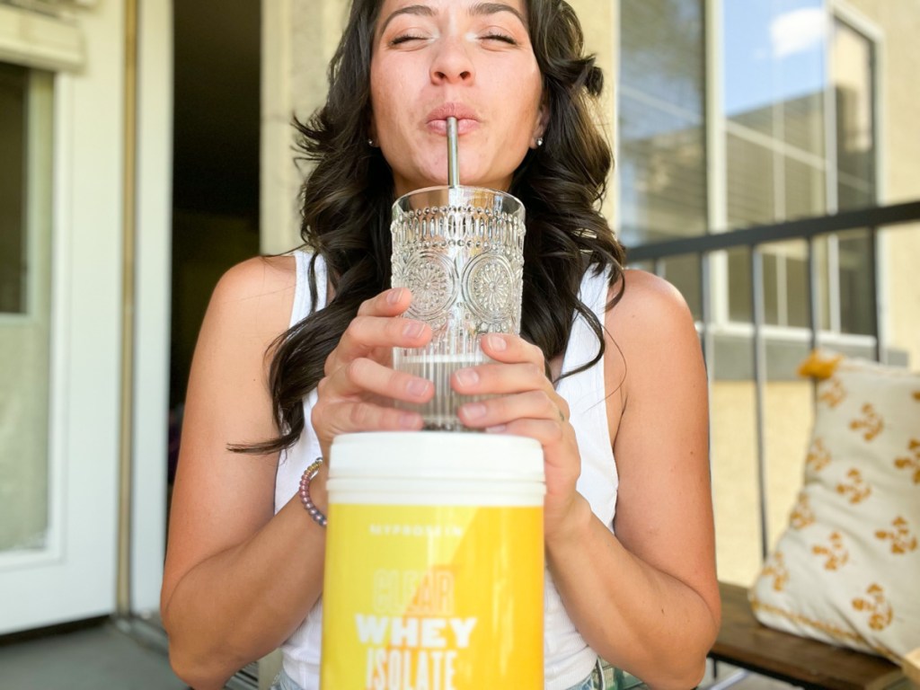 woman sipping straw holding protein powder jug